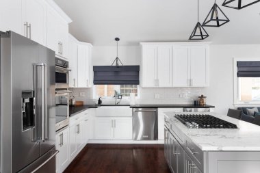 ELMHURST, IL, ABD - 12 HAZİRAN 2021: Modern bir çiftlik evinde güzel beyaz bir mutfak, adanın tavanından sarkan siyah ışıklar, bar tabureleri ve KitchenAid çelik aletleri.