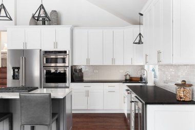 ELMHURST, IL, ABD - 12 HAZİRAN 2021: Modern bir çiftlik evinde güzel beyaz bir mutfak, adanın tavanından sarkan siyah ışıklar, bar tabureleri ve KitchenAid çelik aletleri.
