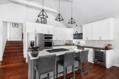 ELMHURST, IL, ABD - 12 HAZİRAN 2021: Modern bir çiftlik evinde güzel beyaz bir mutfak, adanın tavanından sarkan siyah ışıklar, bar tabureleri ve KitchenAid çelik aletleri.