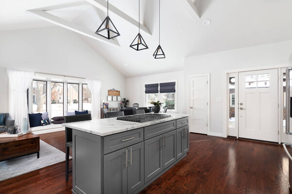 ELMHURST, IL, USA - JANUARY 12, 2021: A modern farmhouse kitchen with a large grey island looking towards an open concept, tall ceiling living and dining room.