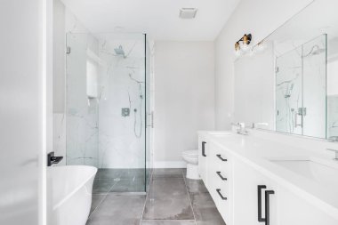 Chicago, IL, ABD - 21 Eylül 2020: siyah donanım ve krom musluklu modern, beyaz bir banyo. Yerden tavana mermer kiremitlerle dolu büyük cam duvarlı bir duş köşede durur..