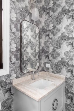 ELMHURST, IL, ABD - 1 Kasım 2020: desenli duvar kağıdı, gri kibir ve mermer tezgahlı modern bir banyo ve bronz ayna üzerinde güzel bir aydınlatma armatürü.