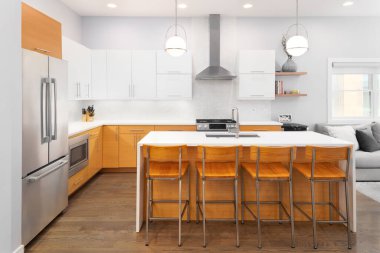 ELMHURST, IL, ABD - 12 Temmuz 2021: Şelale granit adası, ahşap ve beyaz dolapları, paslanmaz çelik aletleri ve ahşap döşemeleri olan lüks bir mutfak.