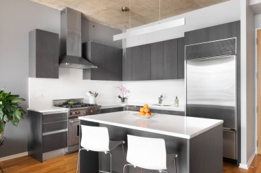 Chicago, IL, ABD - 3 Ocak 2021: Gri dolapları, Wolf ve Sub-Zero paslanmaz çelik aletleri ve adanın beyaz mermer tezgahında oturan beyaz sandalyeli modern bir apartman mutfağı.