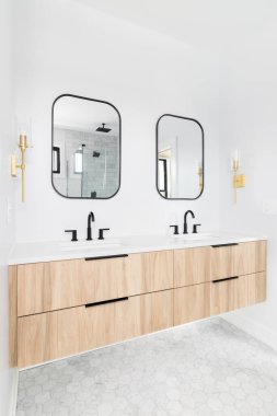 ELMHURST, IL, ABD - 23 Mart 2021: Ahşap bir dolap, siyah çerçeveli ayna ve musluk ve duvara monte edilmiş altın bir ışık ile yenilenmiş bir banyo.
