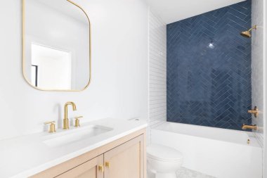 ELMHURST, IL, ABD - 23 Mart 2021: doğal ahşap makyaj dolabı, altın aynası ve muslukları olan yenilenmiş güzel bir banyo ve duş aksanıyla kaplanmış mavi bir ringa kemiği.