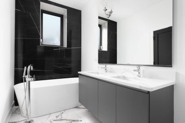 OAK PARK, IL, ABD - 27 Temmuz 2021: Gri makyaj dolabı, beyaz mermer tezgahı, krom musluğu olan ayakta duran küvet ve siyah mermer duvarlı lüks bir banyo.