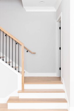 A staircase going up with natural wood steps and handrails, white risers, and wrought iron spindles. clipart