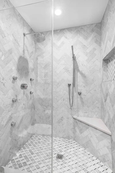 CHICAGO, IL, USA - FEBRUARY 8, 2020: A luxury remodeled shower with marble tiles, a bench seat, and chrome faucets. The wall\'s are covered a herringbone tile pattern.
