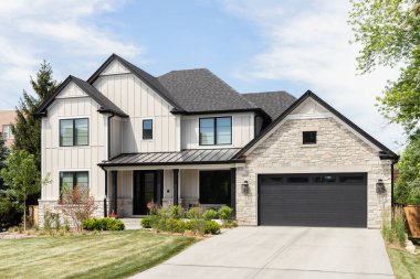 OAK PARK, IL, USA - MAY 30, 2022: A tan modern farmhouse with a wainscoting siding, covered front porch, beautiful landscaping, and stone covered garage.