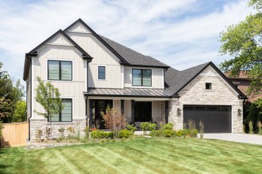 OAK PARK, IL, USA - MAY 30, 2022: A tan modern farmhouse with a wainscoting siding, covered front porch, beautiful landscaping, and stone covered garage.