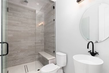 Dairesel aynası, mermer döşemeli duşu ve siyah musluğu olan lüks bir banyo..