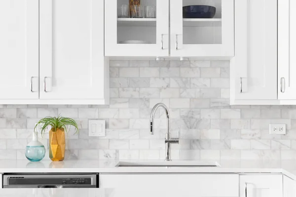 A kitchen sink detail shot with white cabinets, marble subway tile backsplash, and cozy decor.