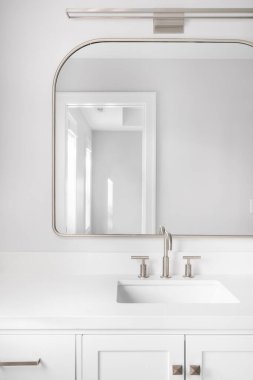 Beyaz bir dolap, bronz ayna, musluk ve mermer tezgah ile çekilmiş bir banyo detayı..