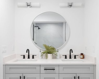 Gri makyaj dolabı olan yenilenmiş bir banyo, duş manzaralı dairesel bir ayna ve arka musluk..