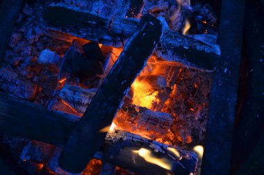 Kömürlerin üzerinde alev alev yanan bir ateş. Yanan mangal kömürünün yakın çekim görüntüsü. Ateşin içinde kızgın kömür. Tasarım için arkaplan.