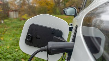 Köyde beyaz elektrikli araba şarj edilir. Şehrin dışında, kırsal kesimde. Özel elektrikli araba şarj aleti. Köy evinde elektrik akımı