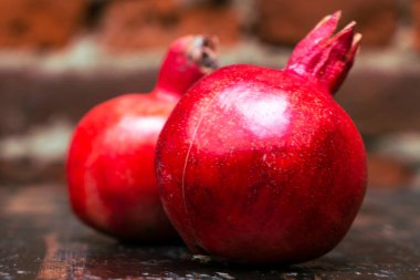 Masada iki kırmızı nar yatıyordu. Kırmızı tuğla duvarlı arka planda masada iki tane olgun taş var. Tüylü yemek. Hayat konsepti.
