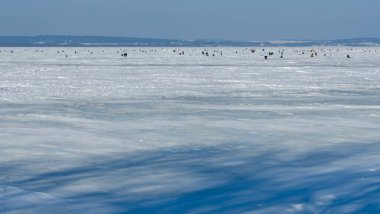Mavi arka planda donmuş gölde kış balıkçılığı yapmak için bir sürü balıkçı. Metin için boşluk.