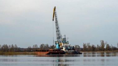 Dredger nehirdeki çim alanını derinleştirmeye çalışıyor. Nehirdeki bir tarakçı tarafından temizleniyor ve derinleşiyor. Nehirde gün batımı. Endüstriyel kavram.