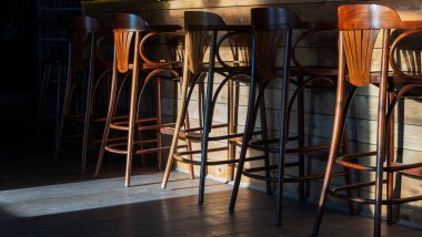 Bir sıra boş ahşap bar taburesi içki kafesinde tezgahın yanında. Güneş ışığında bar sandalyeleri.