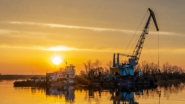 Dredger nehirdeki çim alanını derinleştirmeye çalışıyor. Nehirdeki bir tarakçı tarafından temizleniyor ve derinleşiyor. Nehirde gün batımı. Endüstriyel kavram.