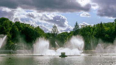 Çeşmeden su. Bulutlu gökyüzünün arkasındaki çeşme akıntısının tepesinde. Nehirdeki çeşme dramatik gökyüzüne karşı. Şehir manzarası görünümü.