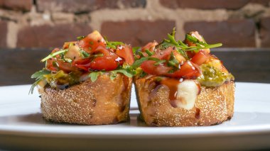 Domates ve mozzarella bruschetta 'nın yakın plan görüntüsü kırmızı tuğlalı arka planda beyaz tabakta..