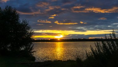 Göldeki şafak güneşinin ışınları. Nehirdeki günbatımı bulutlarının yansıması. Kırsal alan. Panoramik pankart. Panoramik pankart. Doğa konsepti.