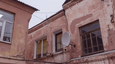 Duvarında yuvarlak bir uydu anteni olan eski bir binanın parçası. Evin arka cephesinde rüzgarlar. Seçici odak.