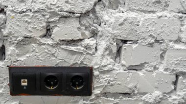 Siyah elektrik prizli beyaz tuğla duvar.