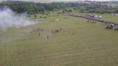 1812 savaşının yeniden inşasına dair geniş bir bakış açısı. Rus ordusu Mir Kalesi yakınlarında Fransızlara saldırıyor. Askerler topları ve tüfekleri ateşler, süvariler dörtnala koşar. Savaş meydanında patlamalar ve kurşunlar. At dövüşü..
