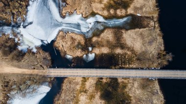 Baharda küçük bir nehrin üzerindeki ahşap köprünün havadan görünüşü.