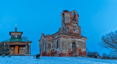 Eski kilise kalıntılarının panoramik manzarası ve günbatımında kar altında modern ahşap şapel..