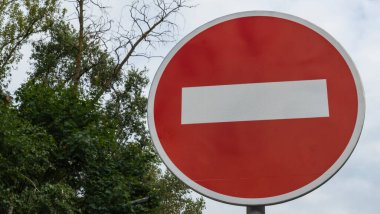 Giriş Trafik İşareti Yok. Beyaz renkli yuvarlak yol işareti ile kırmızı beyaz bulutlu mavi gökyüzü ve yeşil ağaç dalları.