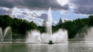 Çeşmeden su. Bulutlu gökyüzünün arkasındaki çeşme akıntısının tepesinde. Nehirdeki çeşme dramatik gökyüzüne karşı. Şehir manzarası görünümü.
