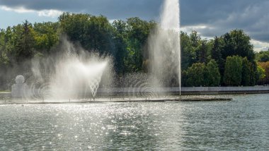 Çeşmeden su. Bulutlu gökyüzünün arkasındaki çeşme akıntısının tepesinde. Nehirdeki çeşme dramatik gökyüzüne karşı. Şehir manzarası görünümü.