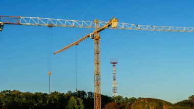Şehir merkezindeki inşaat alanının panoramik manzarası. Mavi arka planda ağır inşaat malzemelerini kaldırmak için birkaç uzun sarı vinç var. İnşaat endüstrisi. Metin için boşluk.