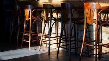 Bir sıra boş ahşap bar taburesi içki kafesinde tezgahın yanında. Güneş ışığında bar sandalyeleri.