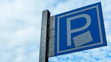 Mavi yol işareti, üzerinde P harfi olan dikdörtgen levha mavi gökyüzüne karşı izole edilmiş. Bulutlu mavi bir arka planda park sembolü. Metin için boşluk.