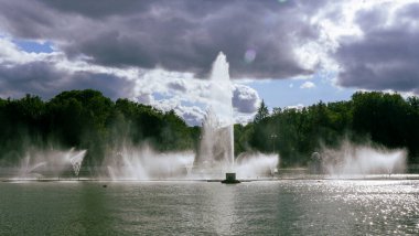 Çeşmeden su. Bulutlu gökyüzünün arkasındaki çeşme akıntısının tepesinde. Nehirdeki çeşme dramatik gökyüzüne karşı. Şehir manzarası görünümü.