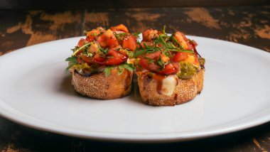 Domates ve mozzarella bruschetta 'nın yakın plan görüntüsü kırmızı tuğlalı arka planda beyaz tabakta..