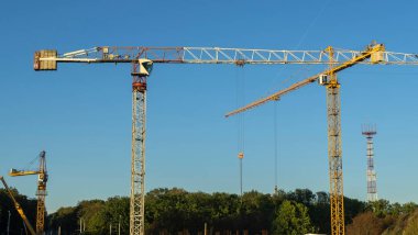 Şehir merkezindeki inşaat alanının panoramik manzarası. Mavi arka planda ağır inşaat malzemelerini kaldırmak için birkaç uzun sarı vinç var. İnşaat endüstrisi.