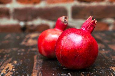Masada iki kırmızı nar yatıyordu. Kırmızı tuğla duvarlı arka planda masada iki tane olgun taş var. Tüylü yemek. Hayat konsepti.