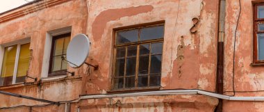 Duvarında yuvarlak bir uydu anteni olan eski bir binanın parçası. Evin arka cephesinde rüzgarlar. Seçici odak.