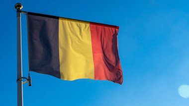 Belçika 'nın ulusal bayrağı mavi gökyüzünün önündeki bayrak direğinde güneş ışınları ve mercek ışığı ile. Diplomasi konsepti. Uluslararası ilişkiler. Metin için boşluk.