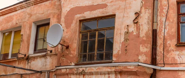Duvarında yuvarlak bir uydu anteni olan eski bir binanın parçası. Evin arka cephesinde rüzgarlar. Seçici odak.