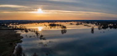 Batan güneşin hava manzarası, sıcak bir bahar akşamında kümülüs bulutlarını yavaşça akan bir nehrin üzerinde yüzdürür. Nehrin üzerinde günbatımı manzarası.