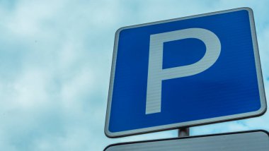 Mavi yol işareti, üzerinde P harfi olan dikdörtgen levha mavi gökyüzüne karşı izole edilmiş. Bulutlu mavi bir arka planda park sembolü. Metin için boşluk.