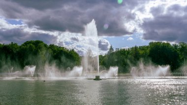 Çeşmeden su. Bulutlu gökyüzünün arkasındaki çeşme akıntısının tepesinde. Nehirdeki çeşme dramatik gökyüzüne karşı. Şehir manzarası görünümü.